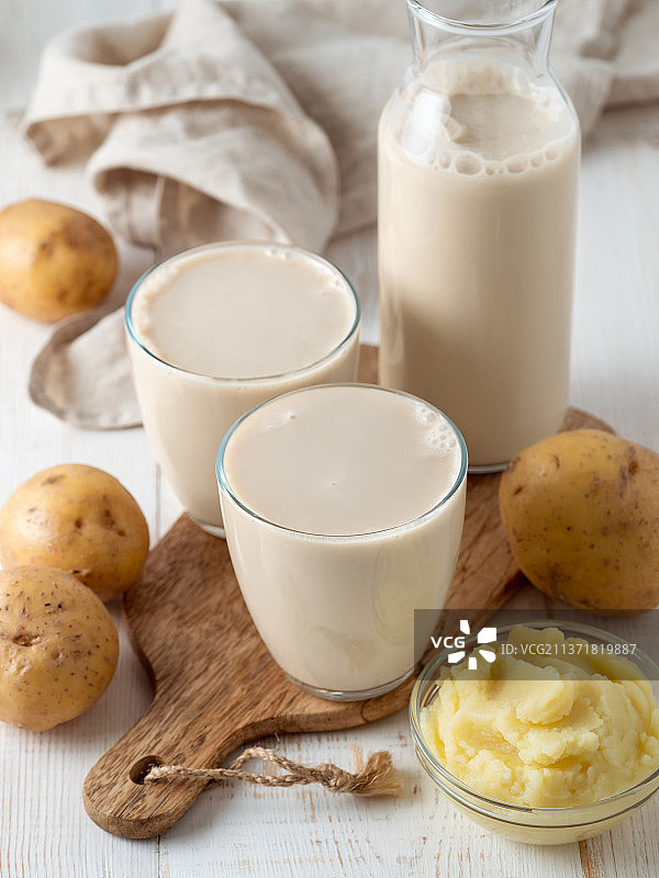 白色木质背景上倒进玻璃杯中的马铃薯奶图片素材