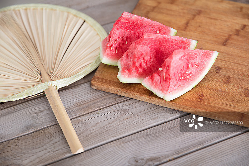 摆在砧板上的几块西瓜和一把老扇子图片素材