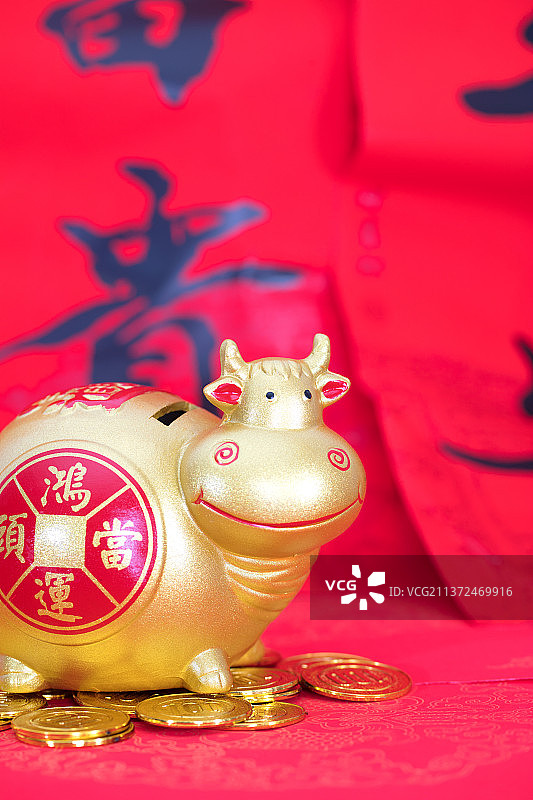 金色的小牛储蓄罐脚踩金币在喜庆的红背景上图片素材