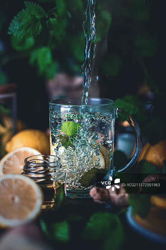 在桌子上将液体水倒入玻璃杯中，制作热柠檬水图片素材