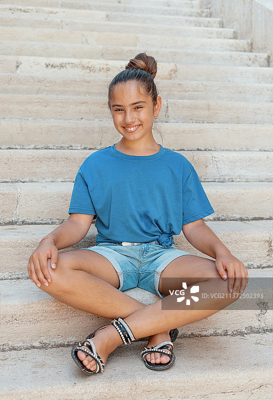 穿着T恤和短裤坐在石阶上的微笑女孩图片素材
