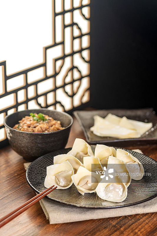 一盘馄饨摆放在中式桌面上旁边有肉馅馄饨皮图片素材