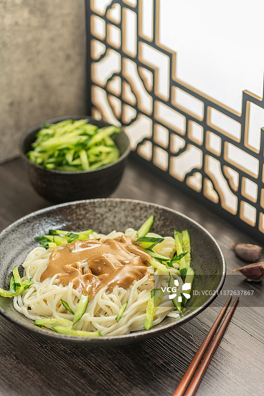 一碗麻酱面摆放在桌面上旁边放有黄瓜丝蒜瓣图片素材