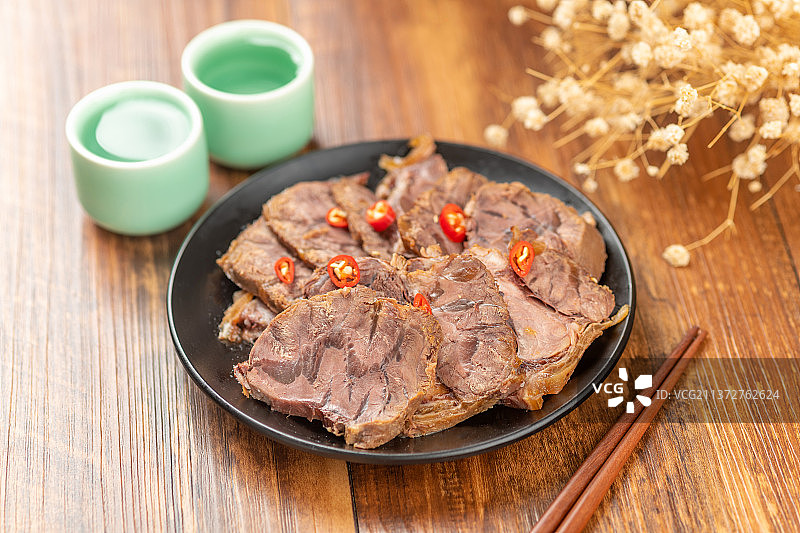 一盘酱牛肉筷子酒杯摆放在木桌面上图片素材