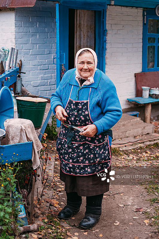 微笑的年老妇女站在房子的肖像，乌克兰图片素材
