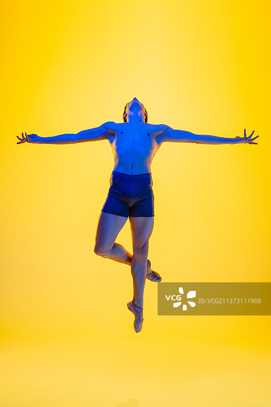 在黄色工作室背景中跳芭蕾舞的年轻优雅舞者图片素材