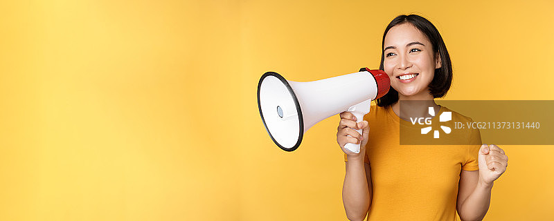 微笑的亚洲女人拿着扩音器站着，宣布事情图片素材