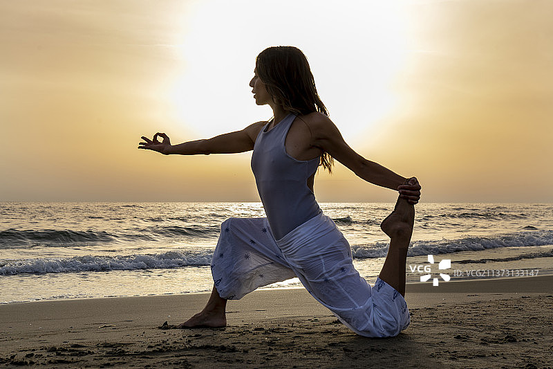 迷人的年轻女人在意大利海边日落时练习瑜伽图片素材