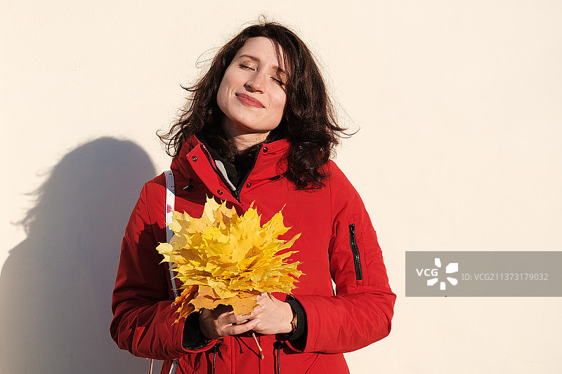 身穿红色外套的女人手持黄色枫叶，俄罗斯图片素材