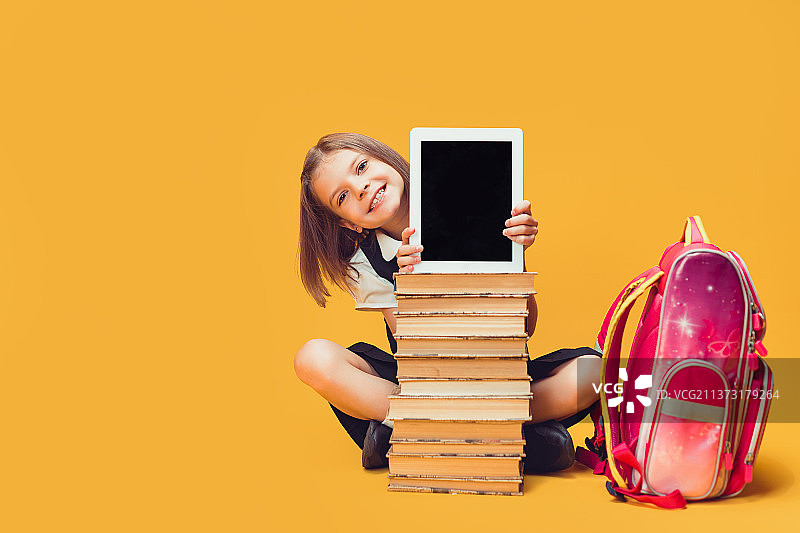 微笑的女学生坐在书堆后展示平板电脑图片素材