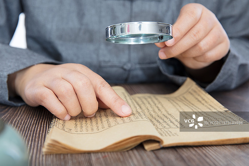 穿着唐装手拿放大镜看书的人图片素材