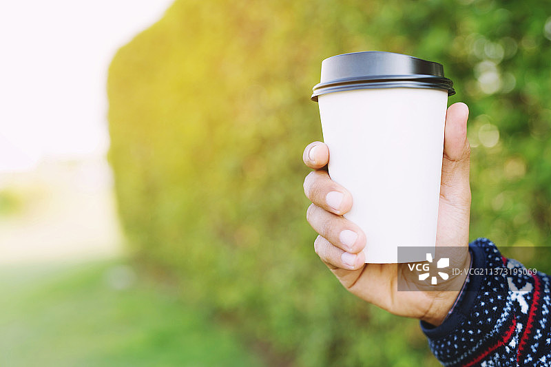 拿着纸杯的年轻的手，拿着一次性杯子靠在树上图片素材