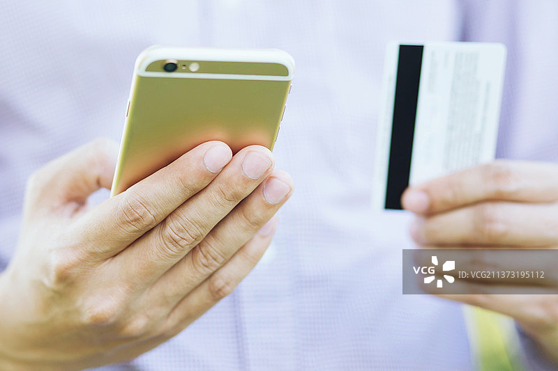 年轻男性的手拿着信用卡，使用手机的中段图片素材