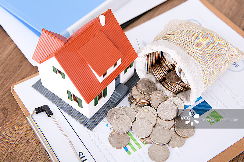 金融文件夹上一个小房子模型和一袋散落的美元硬币图片素材