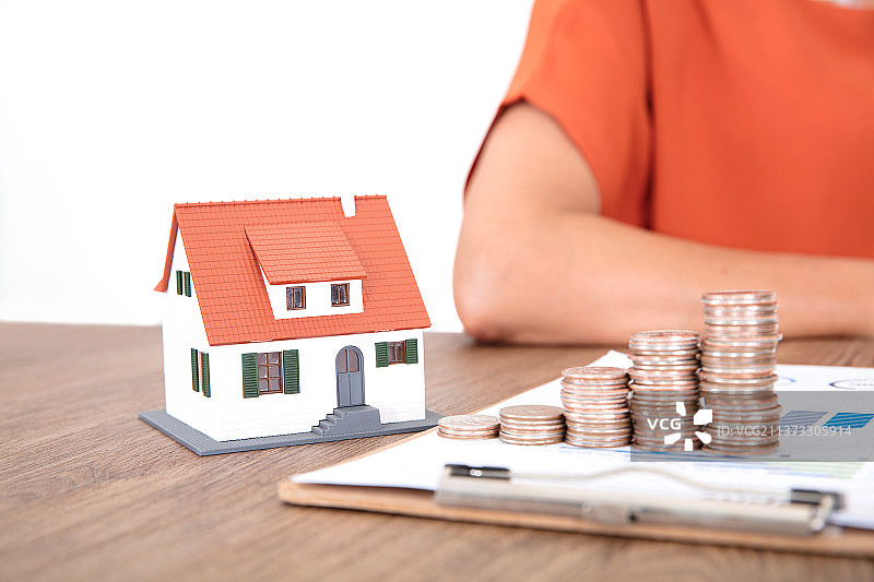 金融文件资料上一排递增的美元硬币和旁边一个小房子模型及坐在桌子旁边的人图片素材