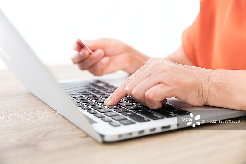老者手拿银行卡敲打笔记本电脑键盘输入图片素材