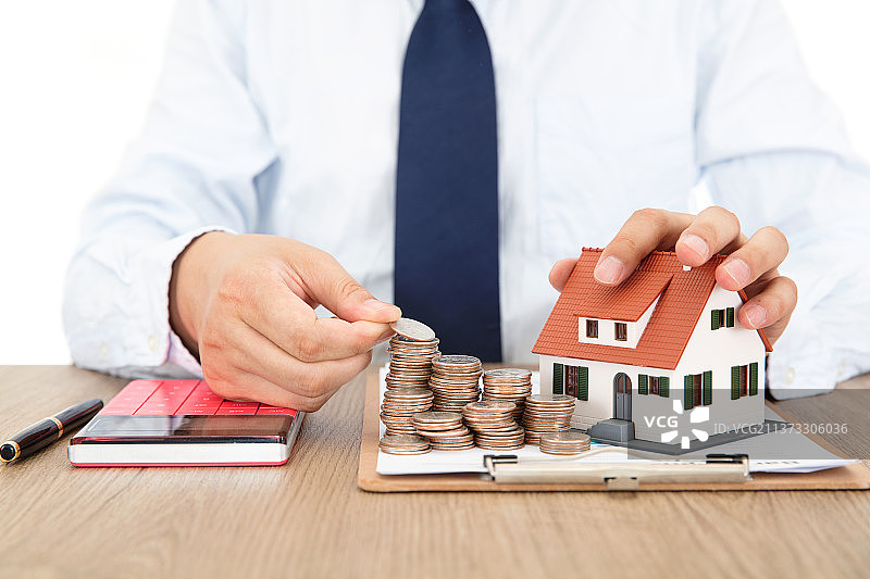 穿正装打领带的商务男性摆放着金融资料上的美元硬币桌上同时还有小房子模型和计算器图片素材