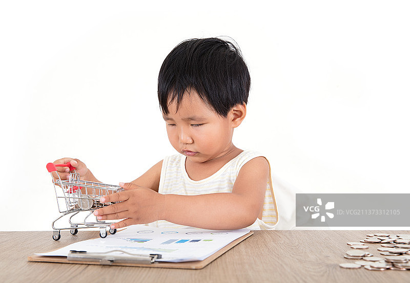 黄皮肤小女孩认真的摆弄上桌子上的购物车模型和一堆美元硬币图片素材
