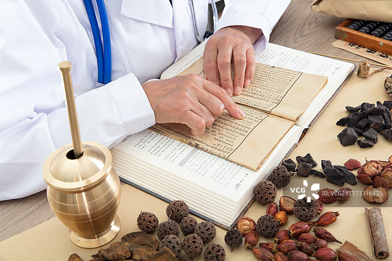 中国老中医趴在摆满草药的桌子上认真看医书图片素材
