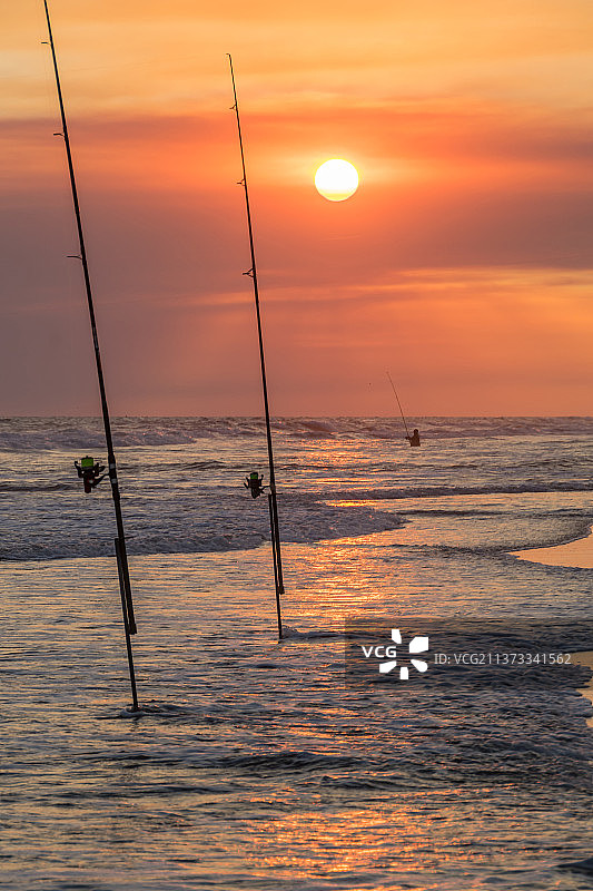 美丽日落时分，沙滩上的钓鱼竿和渔线轮图片素材