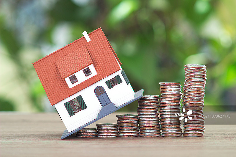绿植背景前面桌子上递增的美元硬币和房屋模型图片素材