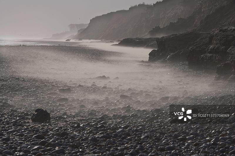 英国萨福克郡科夫海斯海滩上被风吹过的沙滩，卵石半掩在沙中，背景是 Crumbling 悬崖图片素材