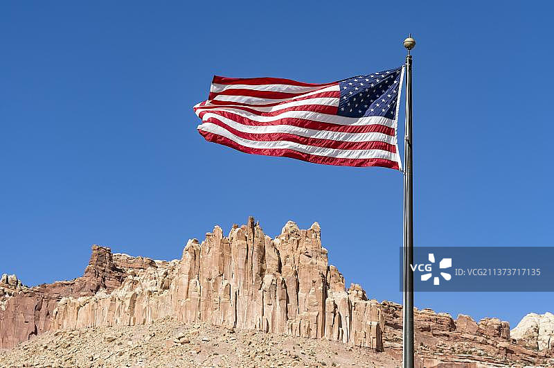 美国国旗在蓝天下飘扬，背后是美国犹他州国会礁国家公园的城堡岩层图片素材
