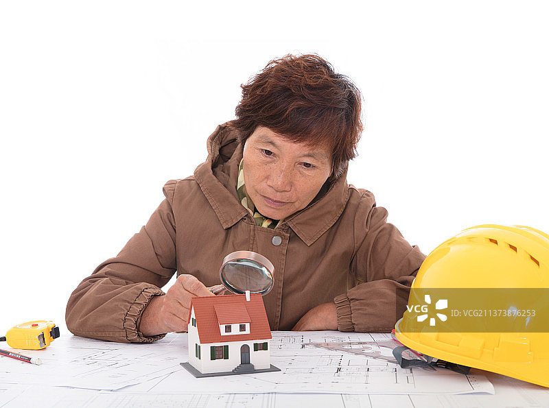 建筑相关从业者手拿放大镜观察满桌子图纸上的房子模型图片素材