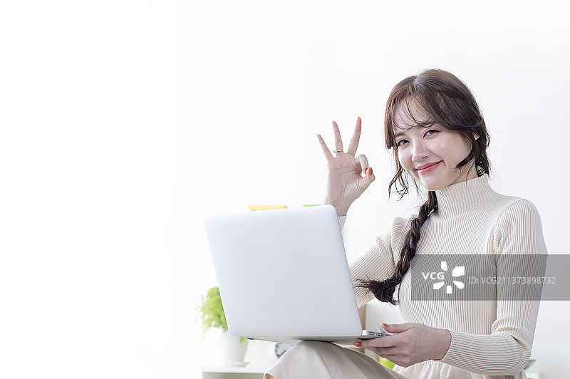 手拿笔记本电脑比同意手势的东方美女图片素材
