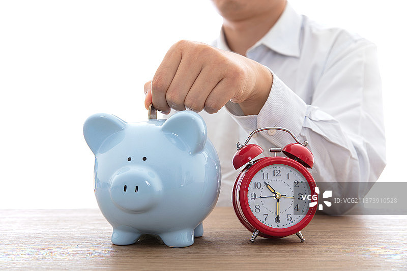 往小猪存钱罐里投硬币和存钱罐旁边一个闹钟图片素材