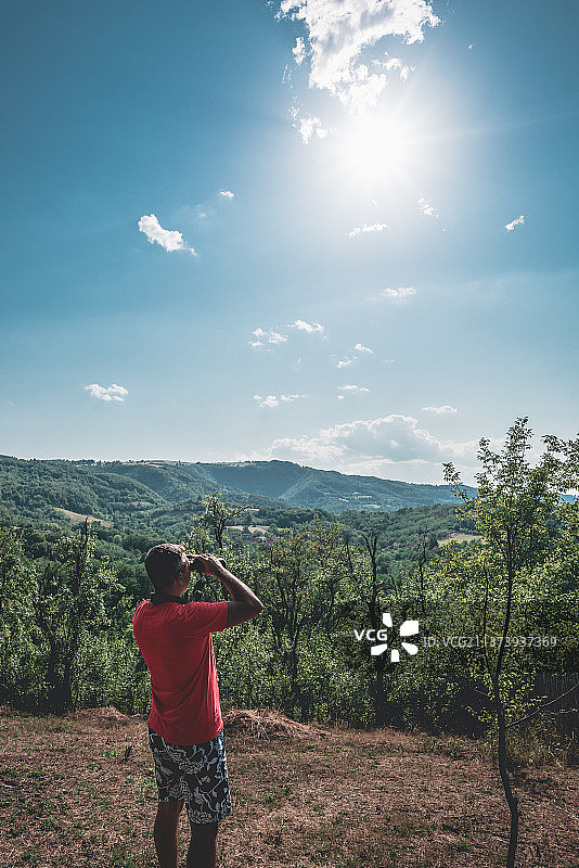 男子使用双筒望远镜观察树木和山丘图片素材