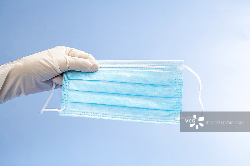 带着防护手套的手拿着口罩特写蓝色背景图片素材