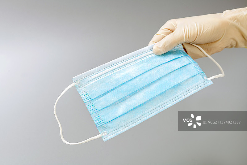 带着防护手套的手拿着口罩特写蓝色背景图片素材