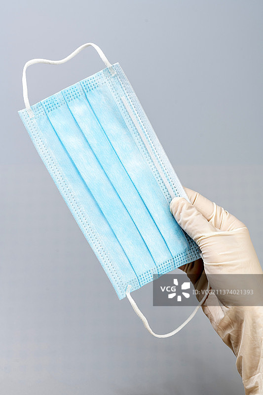 带着防护手套的手拿着口罩特写蓝色背景图片素材