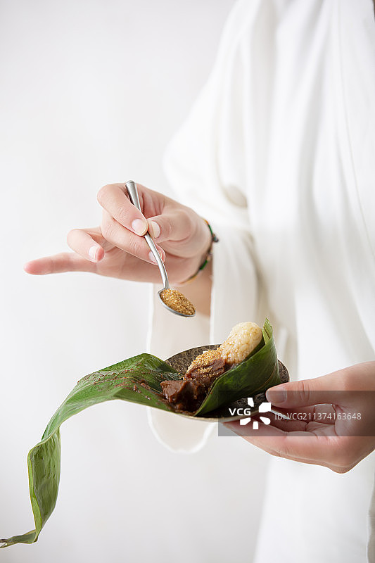 端午节中式国潮禅意静物：穿汉服女子拿着汤匙往豆沙粽子撒砂糖图片素材