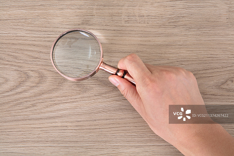 手拿放大镜在桌子上做查看的动作图片素材