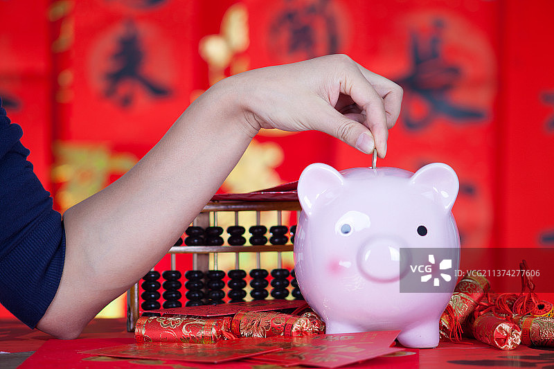 手拿硬币准备投入放在喜庆的红色背景中的小猪存钱罐图片素材