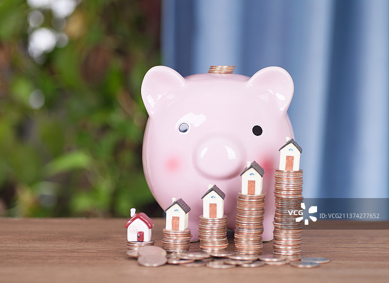 桌子上一排增长的美元硬币顶着一排小房子模型及旁边的小猪存钱罐图片素材