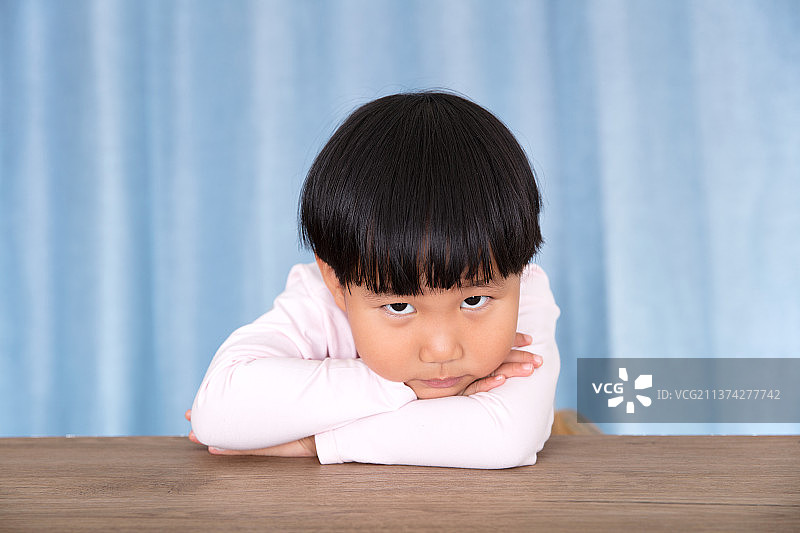 趴在桌子上抬眼看镜头的中国小姑娘图片素材