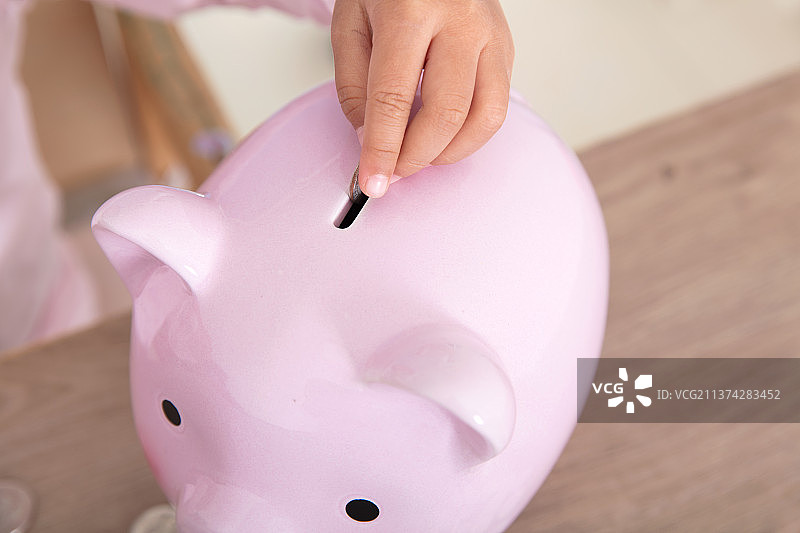 特写拍摄手拿硬币放进小猪存钱罐里图片素材
