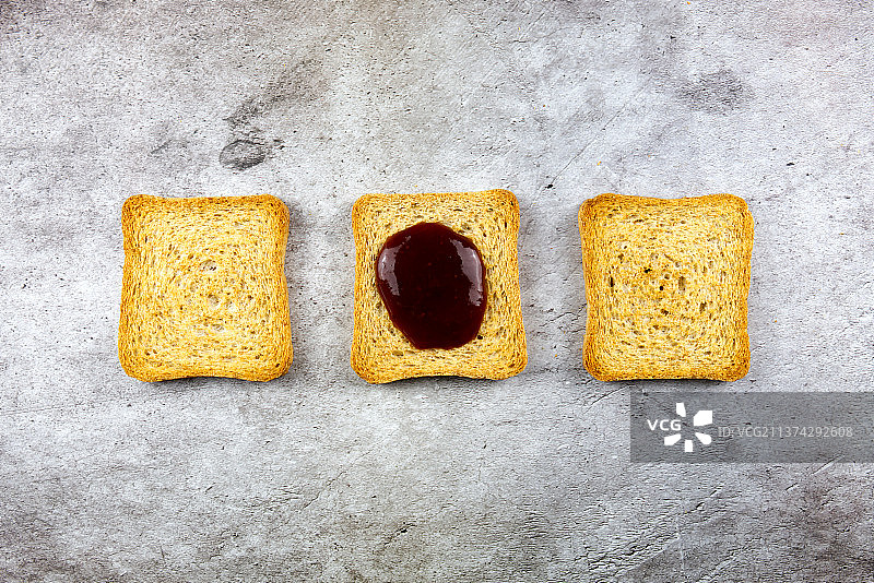 三个面包干切片排成一列，其中一个因有果酱而不同图片素材