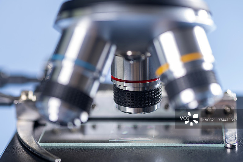 科研人员带着橡胶手套操作显微镜特写蓝色背景图片素材