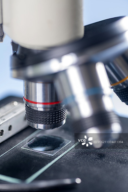 科研人员带着橡胶手套操作显微镜特写蓝色背景图片素材