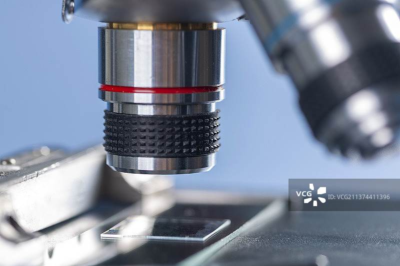 科研人员带着橡胶手套操作显微镜特写蓝色背景图片素材