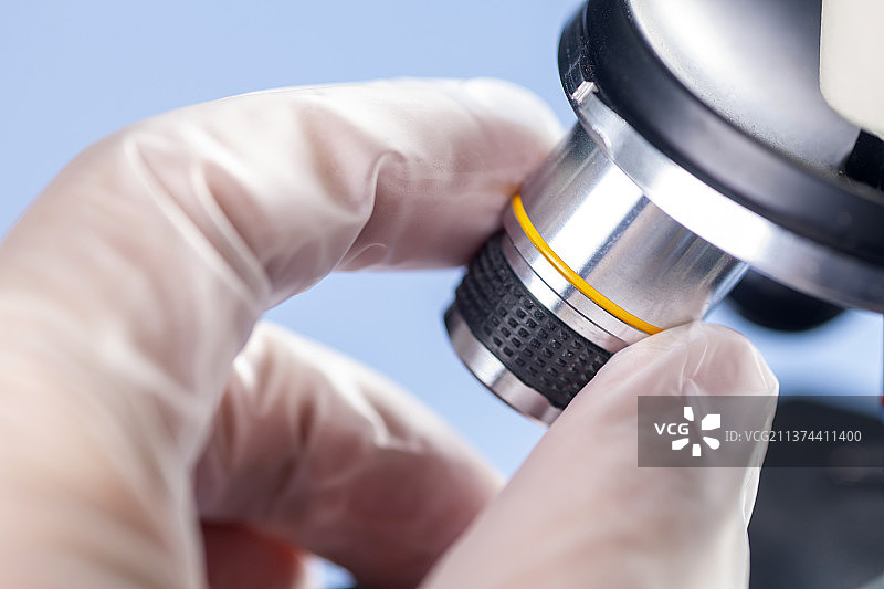 科研人员带着橡胶手套操作显微镜特写蓝色背景图片素材