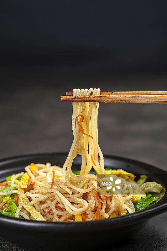 一盘快餐炒米线摆放在黑色背景上图片素材