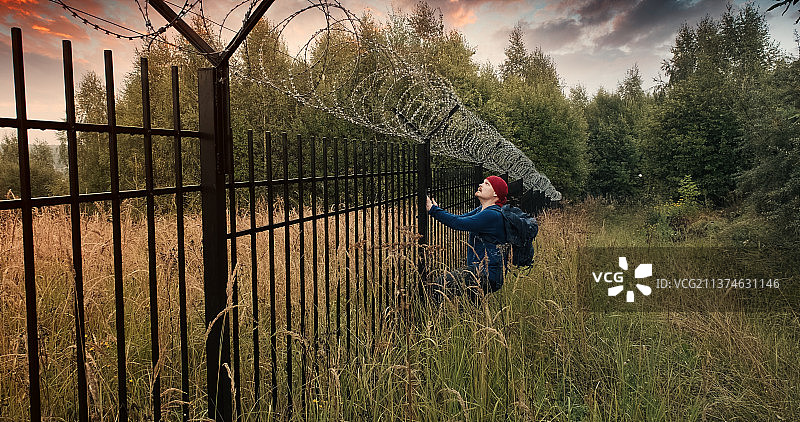 男子跑到带刺铁丝网的栅栏旁并攀爬，傍晚图片素材