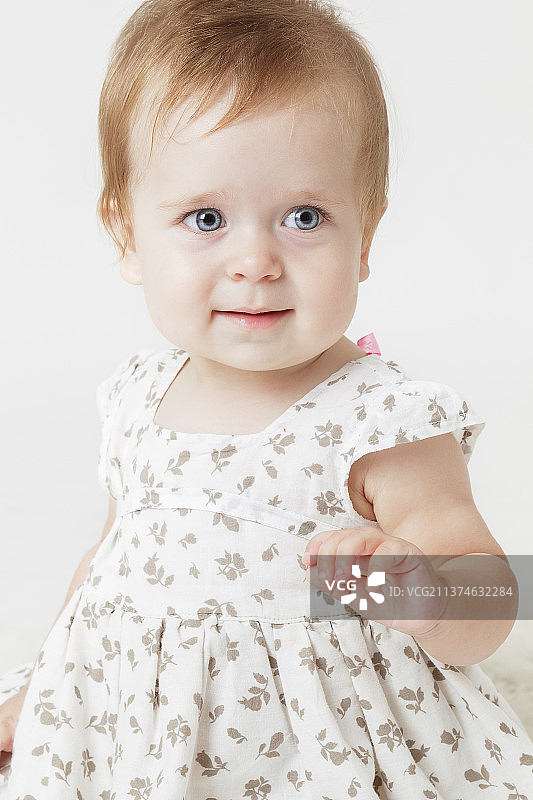 身穿浅色连衣裙、站在浅色背景前的小女孩图片素材