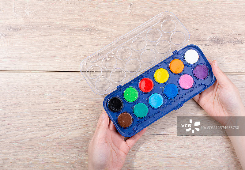 手持木质背景上的水彩颜料盒图片素材