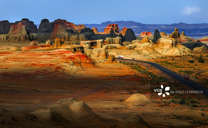 一条公路穿过光影斑驳的雅丹地貌，公路上有汽车在行驶。图片素材